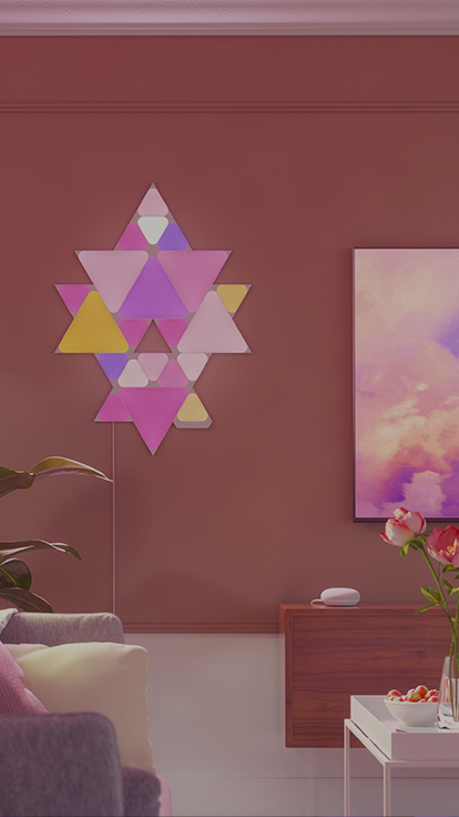 Voici une image d’une disposition de Triangles et Mini Triangles Nanoleaf Shapes montés sur le mur à côté d’un téléviseur dans la salle à manger. Les panneaux lumineux RVB sont reliés entre eux par de connecteurs pour créer un motif.