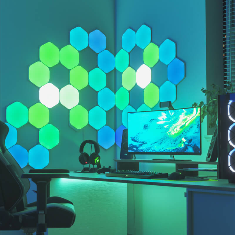 Panneaux lumineux modulaires intelligents Hexagones aux couleurs changeantes et fil compatible Nanoleaf Shapes, montés sur un mur au-dessus d’une battlestation. Produit semblable à Philips Hue, Lifx. HomeKit, Google Assistant, Amazon Alexa, IFTTT.