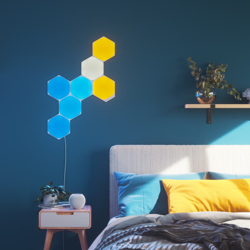 Nanoleaf Shapes Thread enabled color changing hexagon smart modular light panels mounted to a wall in a bedroom. Similar to Philips Hue, Lifx. HomeKit, Google Assistant, Amazon Alexa, IFTTT.