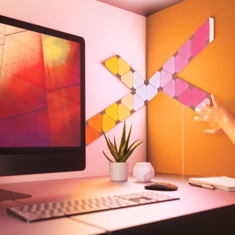 Panneaux lumineux modulaires intelligents Mini triangles aux couleurs changeantes et fil compatible Nanoleaf Shapes, montés sur un mur au-dessus d’un bureau. Produit semblable à Philips Hue, Lifx. HomeKit, Google Assistant, Amazon Alexa, IFTTT.